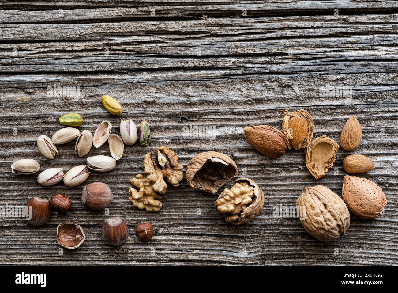 Draufsicht, auf einem alten Holztisch, im Vordergrund einige Walnüsse, Mandeln, Haselnüsse und Pistazien mit und ohne Muscheln. Kopierbereich. Stockfoto