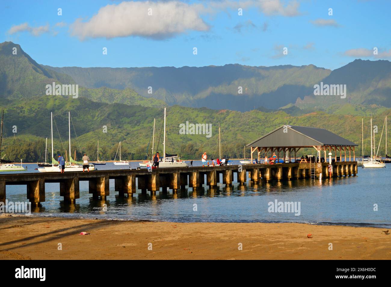Die Menschen genießen es, auf einem Pier in Hanalei Hawaii auf Kauai zu spazieren und einen Blick auf die Hanalei Bay, die umliegenden Berge und Segelboote zu werfen Stockfoto