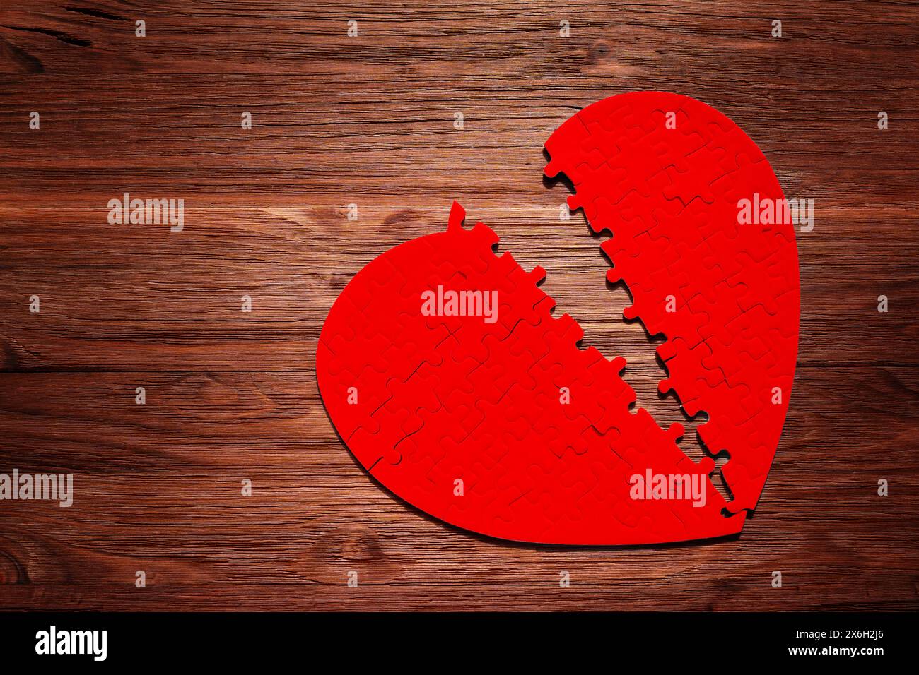 Rotes, herzförmiges Puzzle, in zwei Teile unterteilt, auf dunklem Holzhintergrund. „Liebe, Herzschmerz, Herausforderungen und das Finden von Ganzheit“-Konzept. Stockfoto