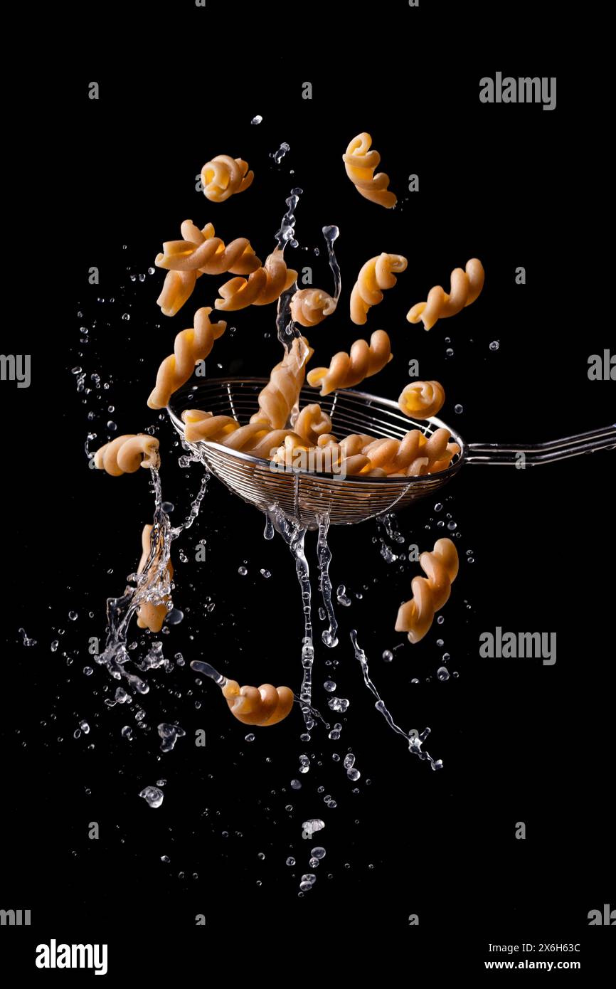 Vollkornfusilli, italienische Pasta, die auf schwarzem Hintergrund schwimmt und tropft. Stockfoto