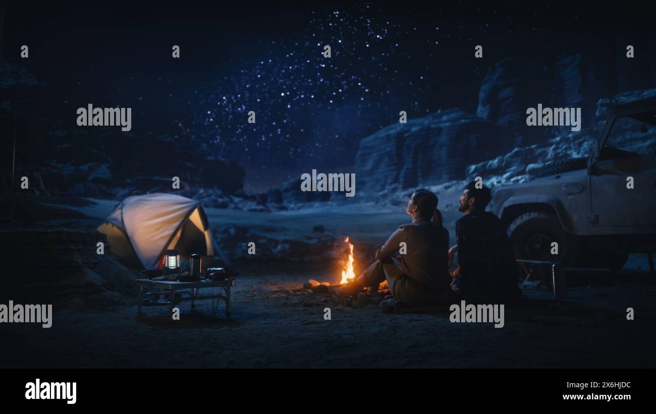 Happy Pair Zelt Camping im Canyon, am Lagerfeuer sitzen und den Nachthimmel mit der Milchstraße voller heller Sterne beobachten. Zwei verliebte Reisende auf einem romantischen Urlaub. Rückansicht Aufnahme Stockfoto