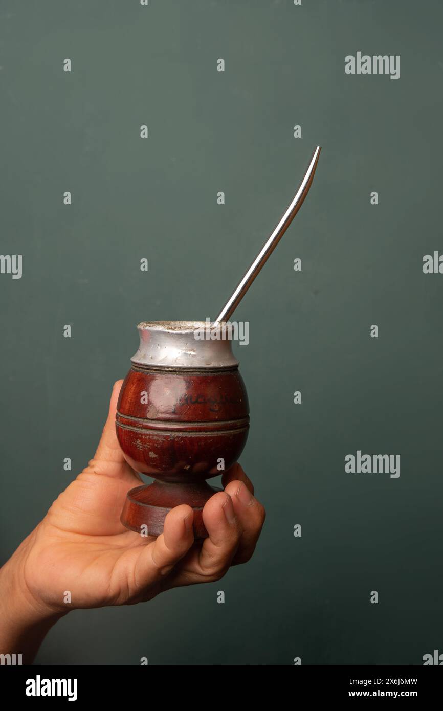 Eine Hand, die einen Mate mit Yerba Mate hält, traditionelles brasilianisches, paraguayisches, argentinisches Uruguar, Heißgetränk, auf grünem Hintergrund Stockfoto