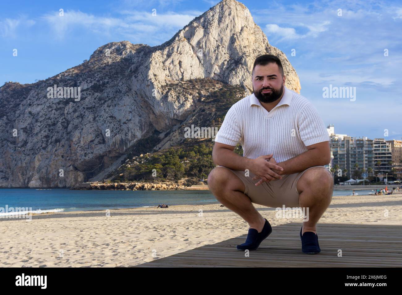 Dieses eindrucksvolle Bild fängt einen 30-jährigen Mann in einem Moment der Reflexion ein, während sich der majestätische Ifach Rock im Hintergrund erhebt. Stockfoto