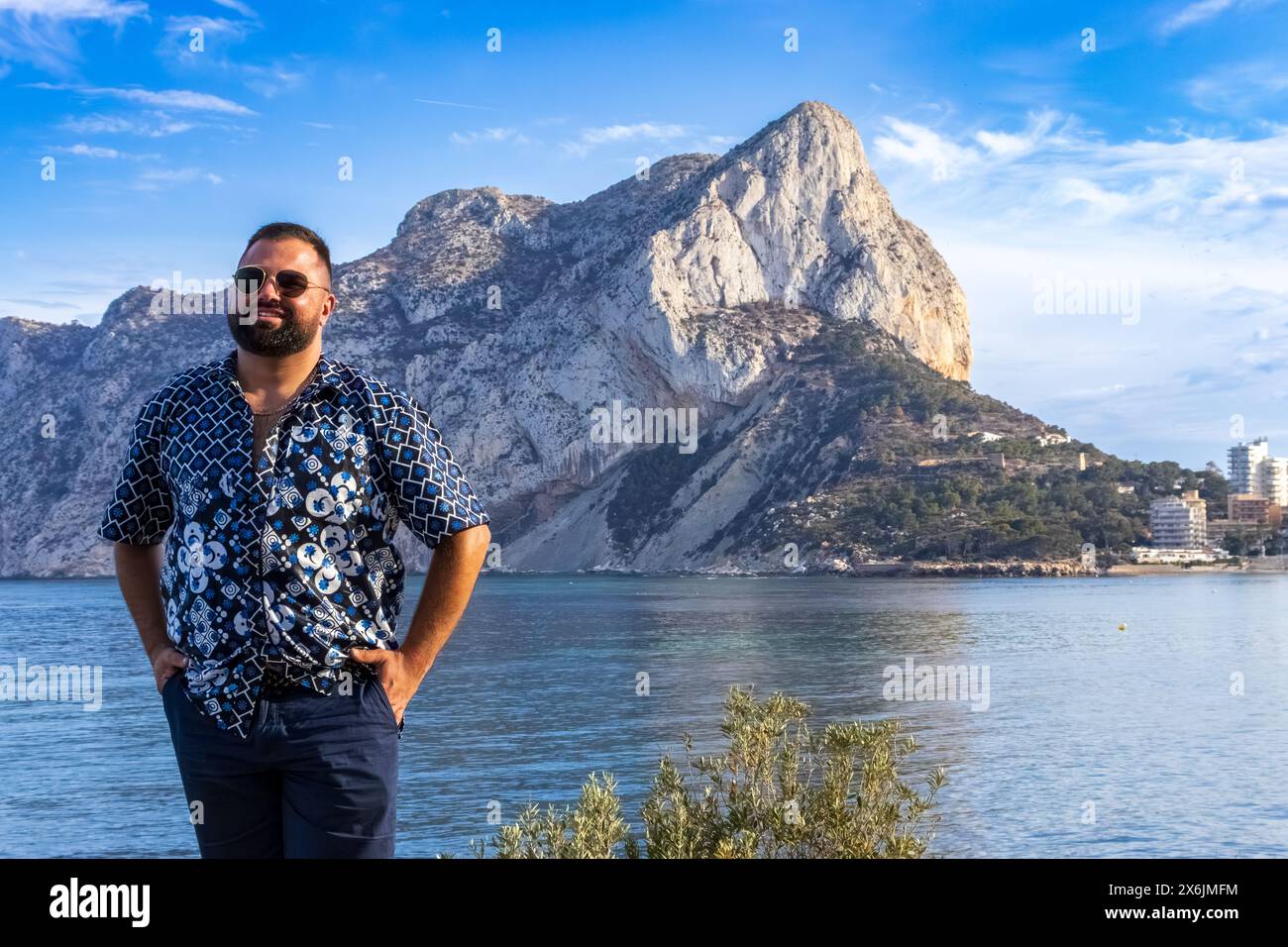 Dieses Porträt fängt einen 30-jährigen Mann ein, der in besinnlicher Einsamkeit mit dem ikonischen Ifach Rock von Calpe, Spanien, steht. Stockfoto