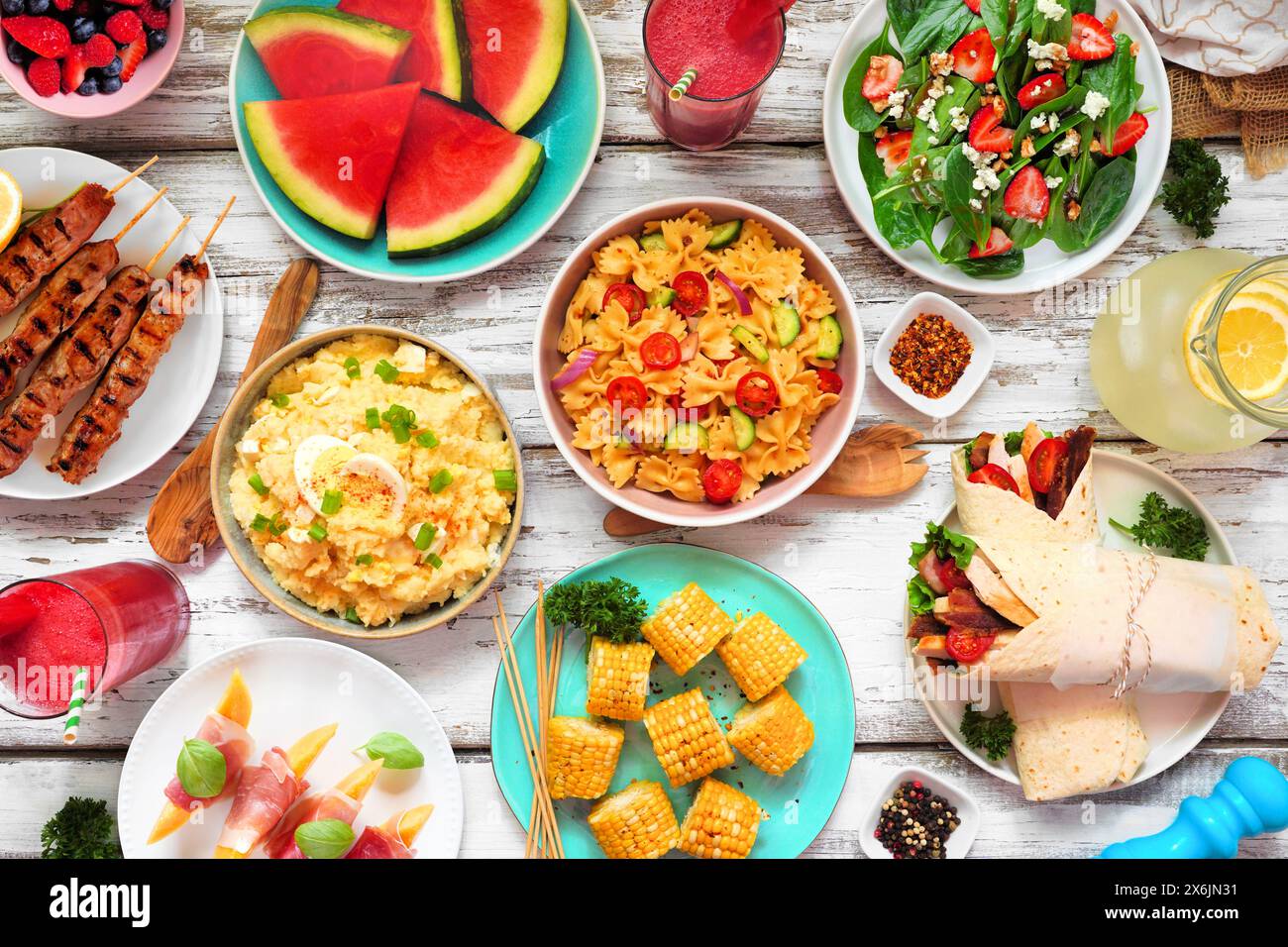 Sommer-Esstisch-Szene auf weißem Holz Hintergrund. Verschiedene erfrischende Salate, Obst, Wraps und Grillspieße. Draufsicht. Stockfoto