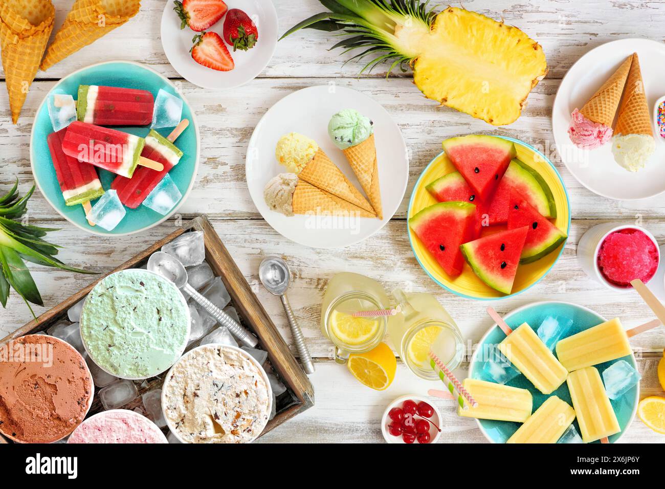 Erfrischende Sommer-Food-Tischszene. Verschiedene Eissorten, Eis und Obst. Blick von oben über einen rustikalen weißen Holzhintergrund. Stockfoto