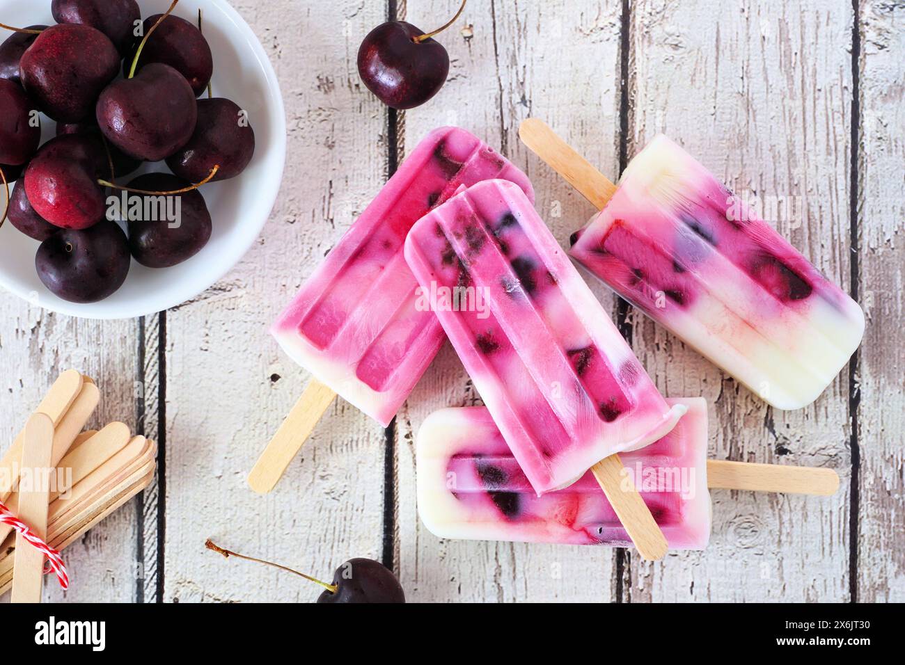 Gesunde Kirschjoghurt-Stiele. Tischszene mit Blick von oben über einem rustikalen weißen Holzhintergrund. Stockfoto