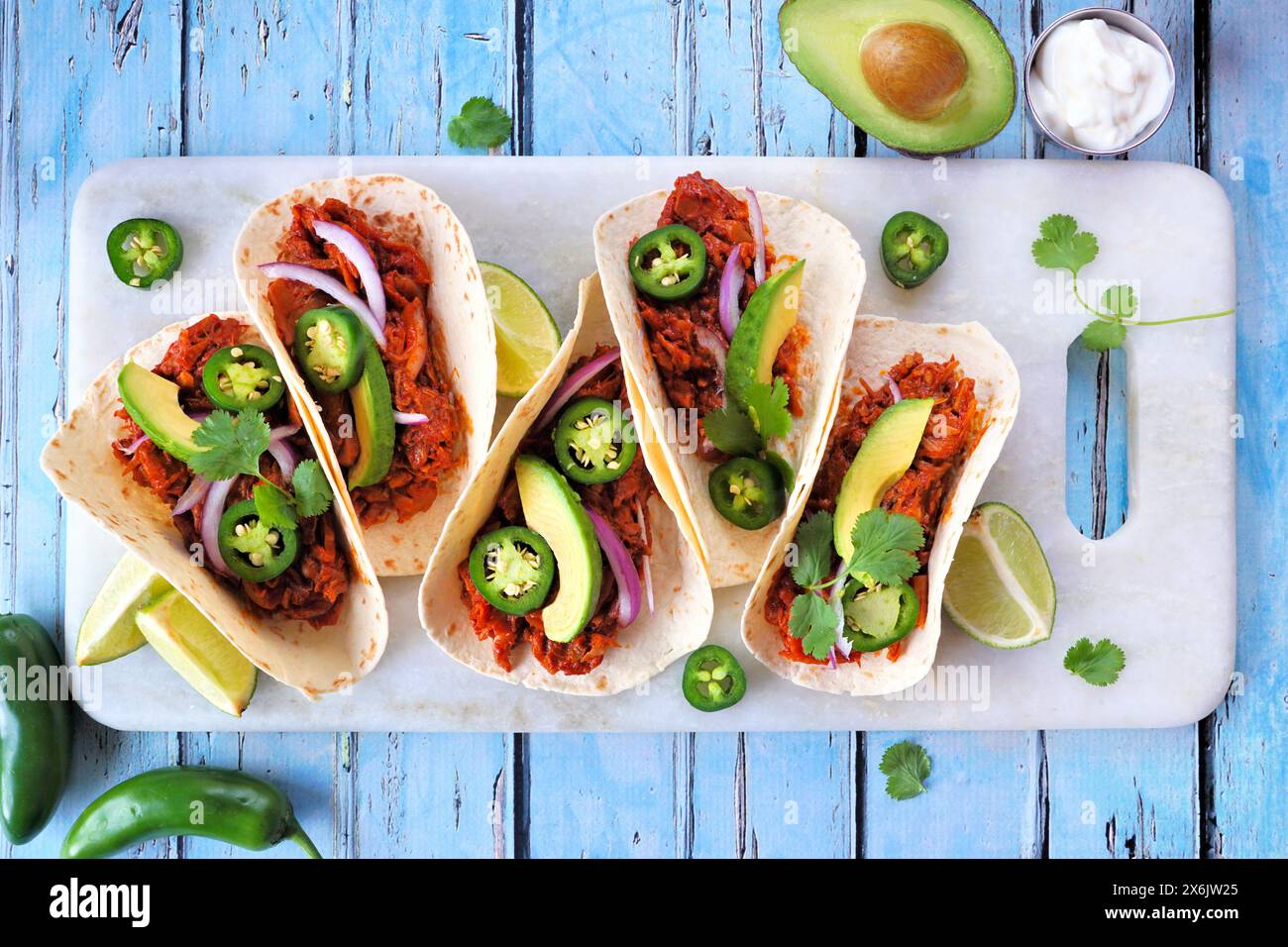 Jack Fruit vegane Tacos. Top-Down-Tischszene über einem rustikalen blauen Holzhintergrund. Gesunde Ernährung, pflanzlicher Pulled Schweinefleisch Ersatz. Stockfoto
