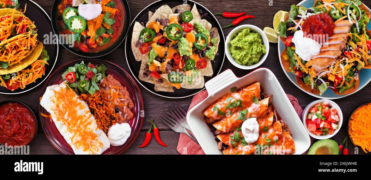 Mexikanische Tischszene. Ansicht von oben nach unten auf einem dunklen Holzbanner Hintergrund. Tacos, Burrito-Teller, Nachos, Enchiladas, Tortilla-Suppe und Salat. Stockfoto