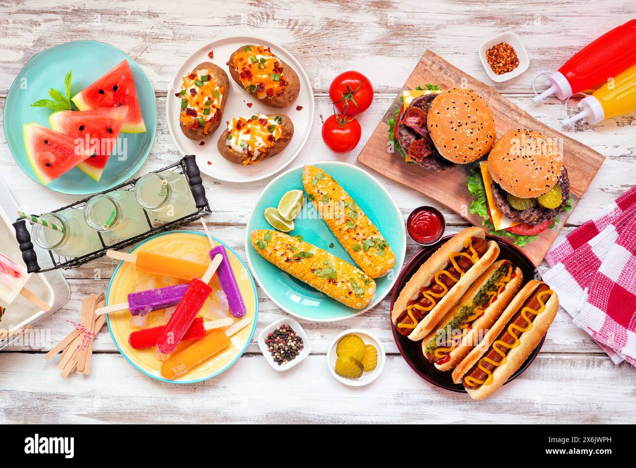 Grilltisch im Sommer. Hamburger, Hot Dogs, Kartoffeln, Mais und kalte Leckereien. Blick von oben über einen weißen Holzhintergrund. Stockfoto