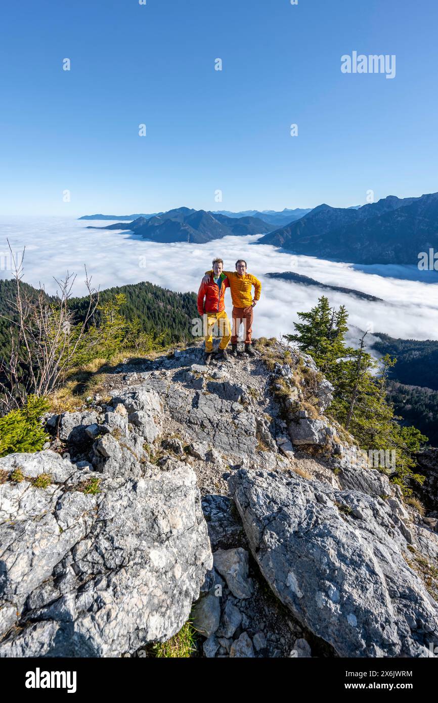 Zwei Freunde legen sich die Arme um die Schultern, Bergsteiger auf dem felsigen Gipfel des Ettaler Manndl, Blick über die Berglandschaft und Stockfoto