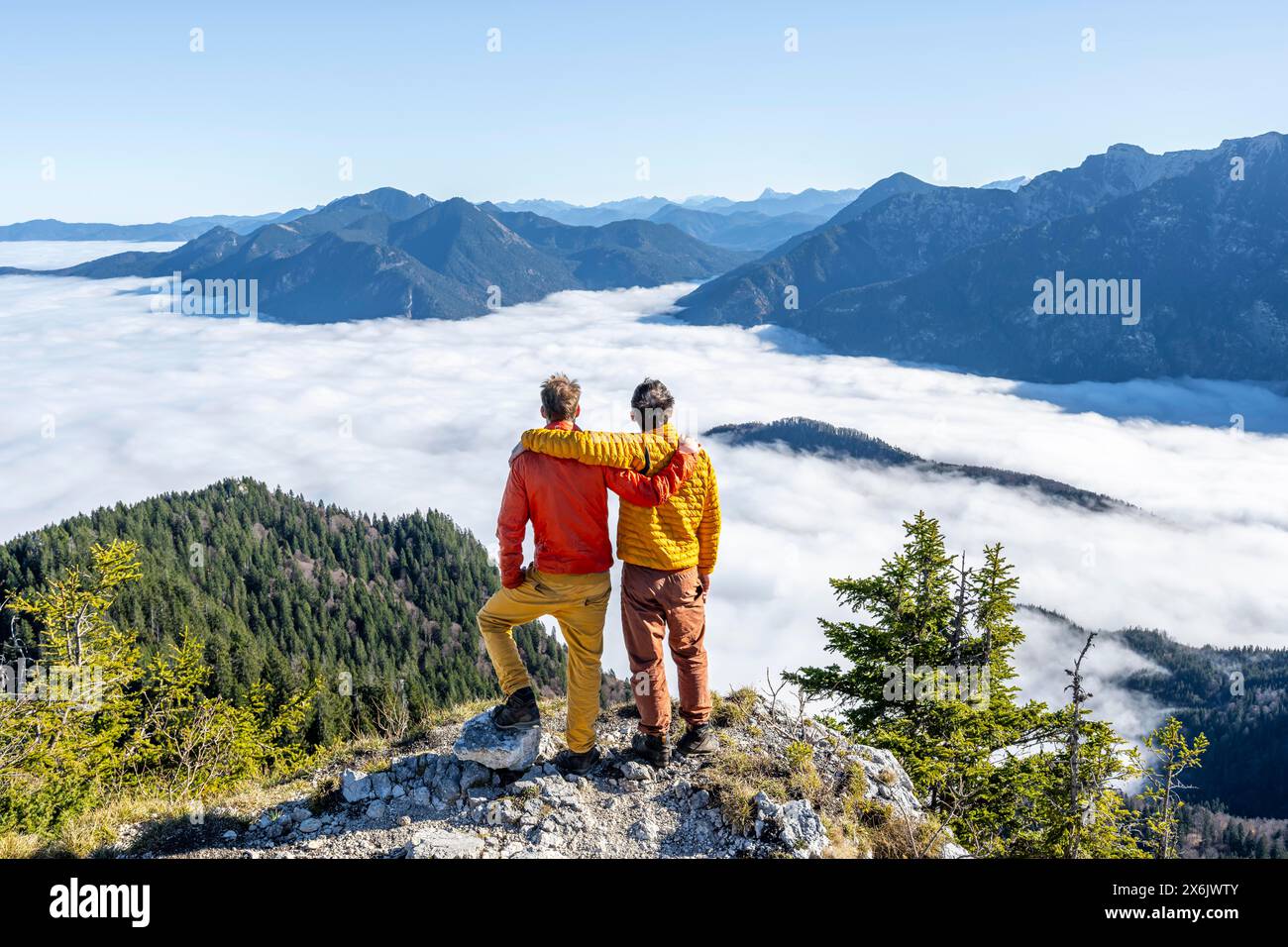 Zwei Freunde legen sich die Arme um die Schultern, Bergsteiger auf dem felsigen Gipfel des Ettaler Manndl, Blick über die Berglandschaft und Stockfoto