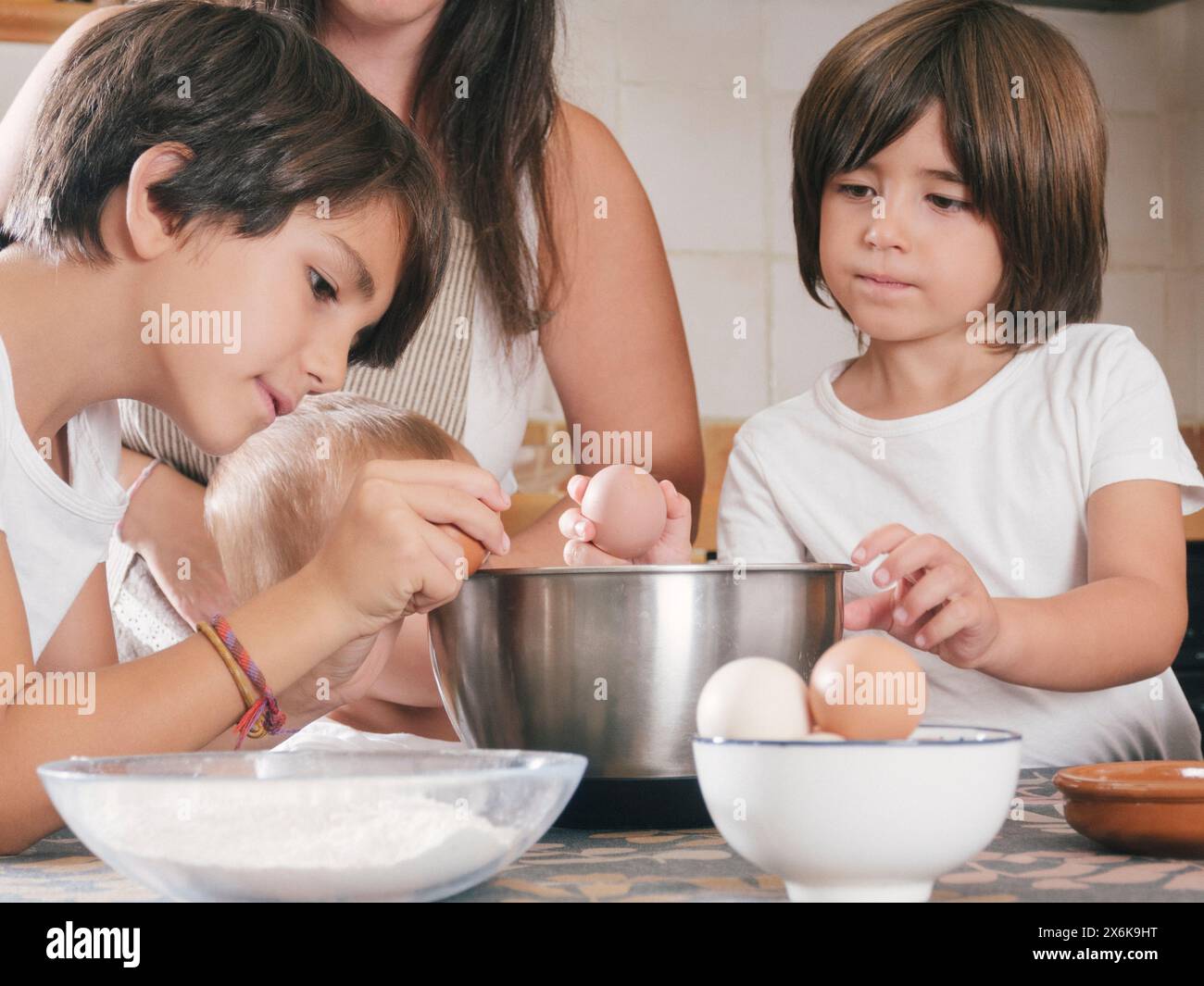 Eine dreiköpfige Familie und eine Frau machen zusammen Frühstück. Die Kinder knacken Eier in eine Schüssel, während die Frau zusieht. Szene ist Krieg Stockfoto