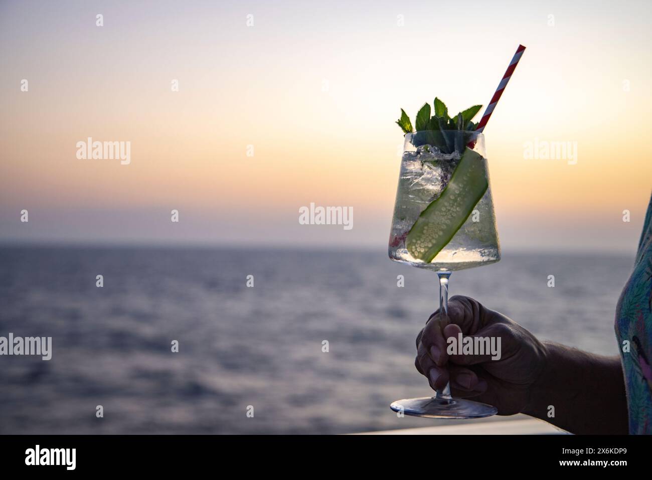 Hand mit Gin Tonic Cocktail auf dem Geländer des Expeditionskreuzfahrtschiffes SH Diana (Swan Hellenic) im Roten Meer bei Sonnenuntergang, auf See, in der Nähe von Saudi Stockfoto