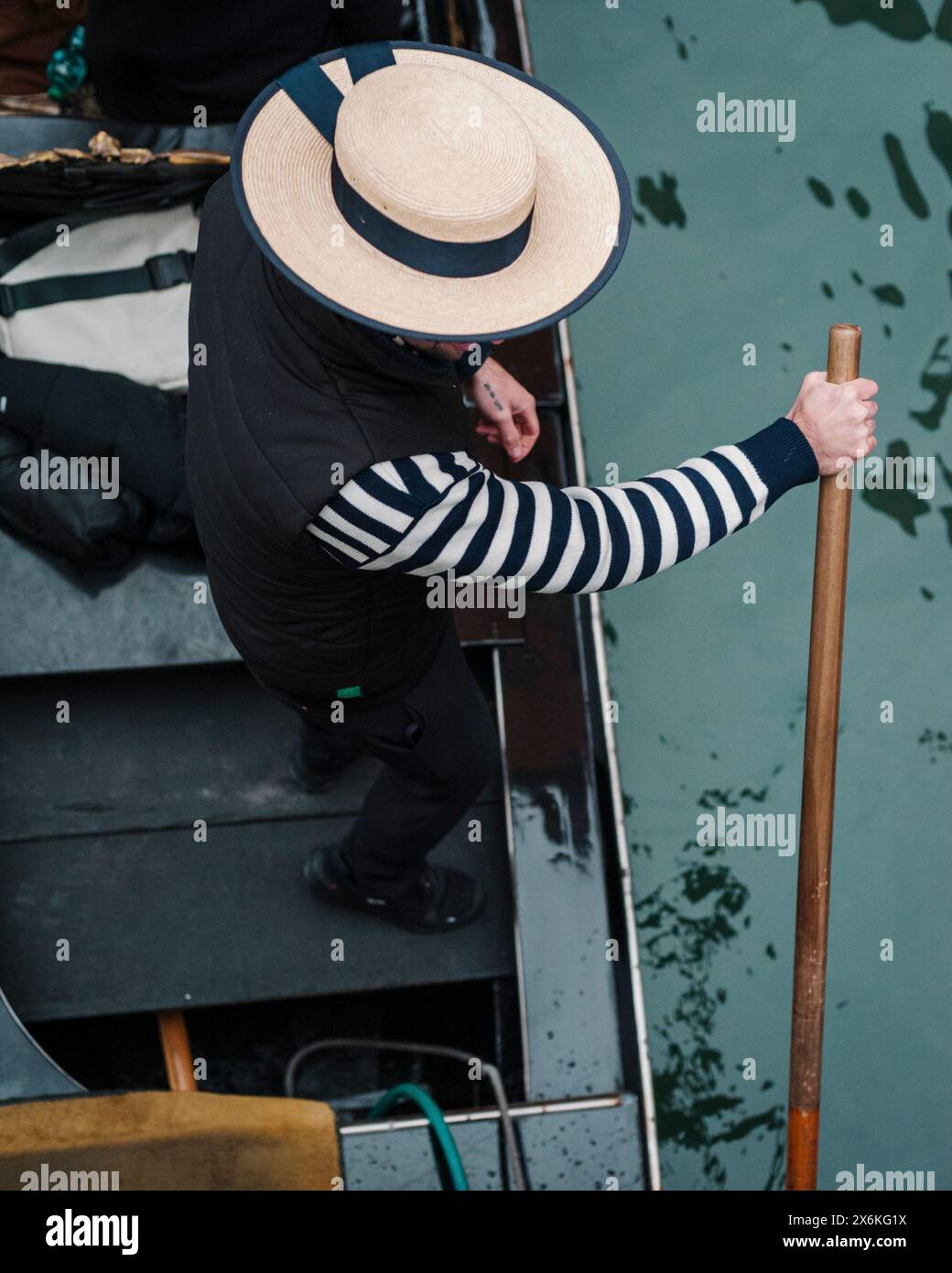 Ein Gondoliere fährt durch die Kanäle von Venedig in Italien mit traditionellem Kanu-Strohhut und gestreiftem Pullover. Stockfoto