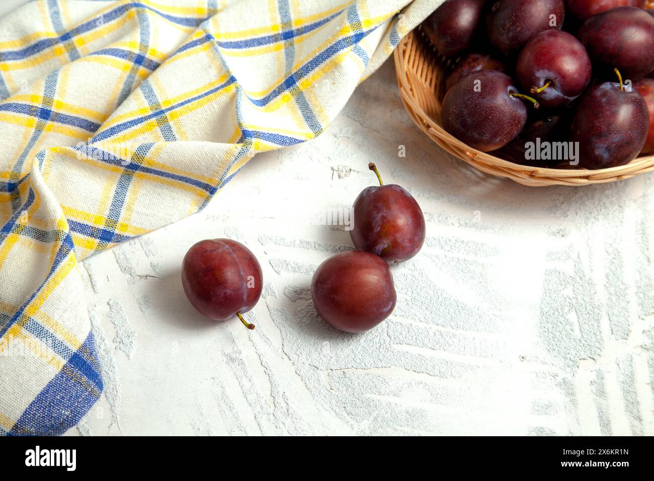 Saftige Sommerpflaumenfrüchte. Mehrere reife süße Pflaumen auf weißem hölzernem Hintergrund mit blauem Küchentuch. Stockfoto