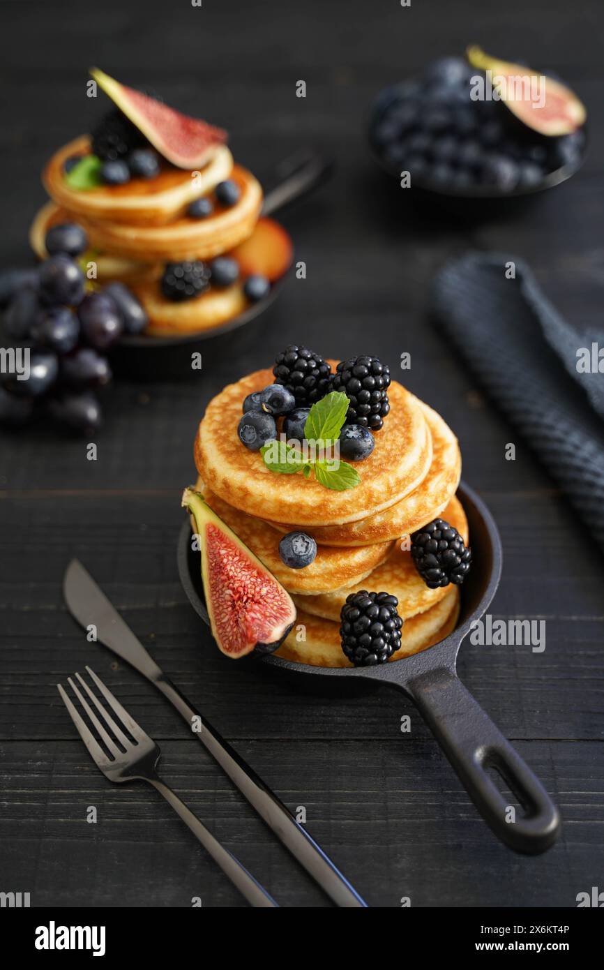 Goldbraune Pfannkuchen vor einem eleganten schwarzen Holzhintergrund mit saftigen Beeren, die Wärme und Genuss ausstrahlen Stockfoto