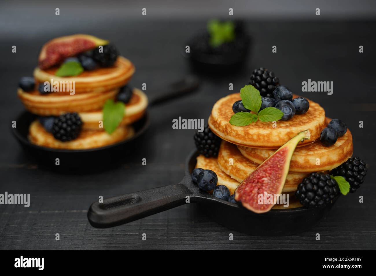 Goldene Pfannkuchen, geschmückt mit leuchtenden Beeren, bilden einen wunderschönen Kontrast zu einem schwarzen Holzhintergrund Stockfoto