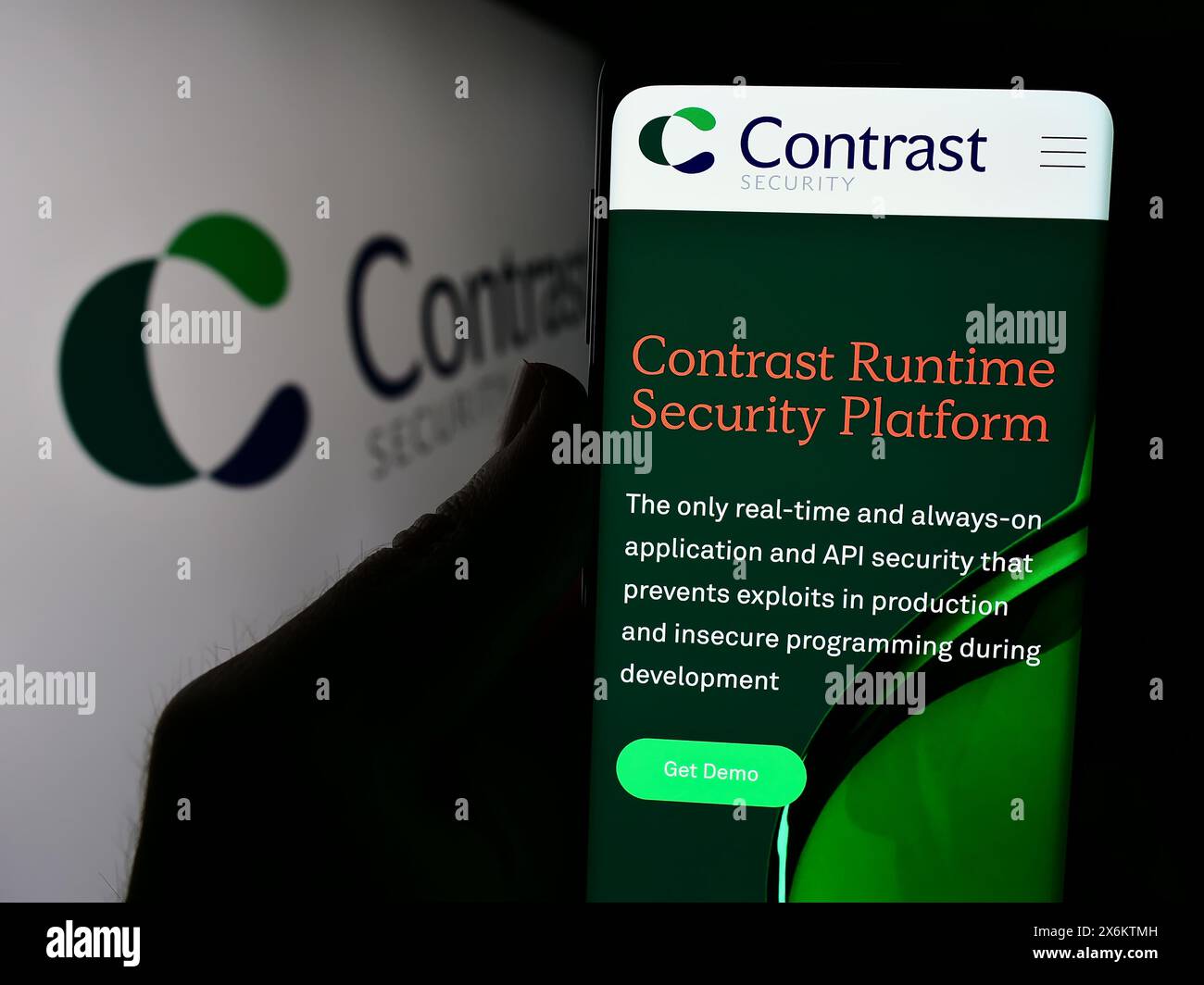 Person, die ein Mobiltelefon hält, mit der Webseite des US-Softwareunternehmens Contrast Security Inc. Vor dem Firmenlogo. Konzentrieren Sie sich auf die Mitte des Telefondisplays. Stockfoto