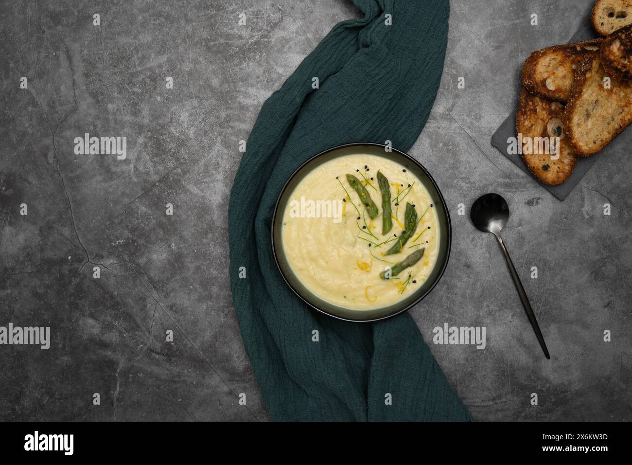 Eine Schüssel mit samtiger weißer Spargelsuppe, elegant garniert mit leuchtend grünen Spargelsprossen Stockfoto