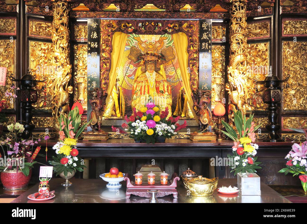 Ein prächtiger goldener Altar mit Blumenschmuck und Opfergaben in der Kaiserin-Zhusheng-Halle im Dalongdong Baoan-Tempel, Taipeh, Taiwan Stockfoto