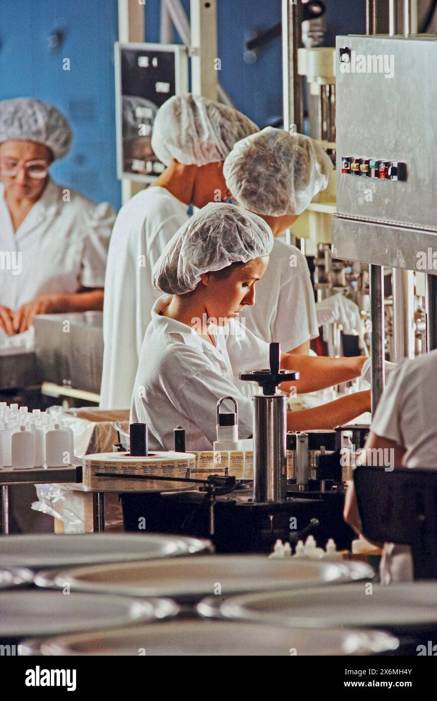 Eine Gruppe verschiedener Personen in einer pharmazeutischen Produktionsanlage, die Schutzausrüstung tragen und gemeinsam Maschinen und Produkte bedienen Stockfoto