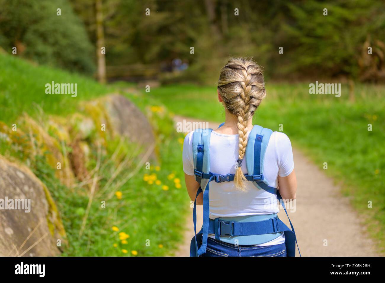 Rückansicht einer blonden Frau, die mit ihrem kleinen Baby durch einen Park in der Natur geht Stockfoto