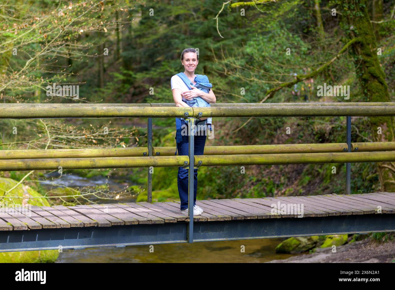 Schöne blonde Frau, die mit ihrem kleinen Baby auf einer Brücke in der Natur steht Stockfoto