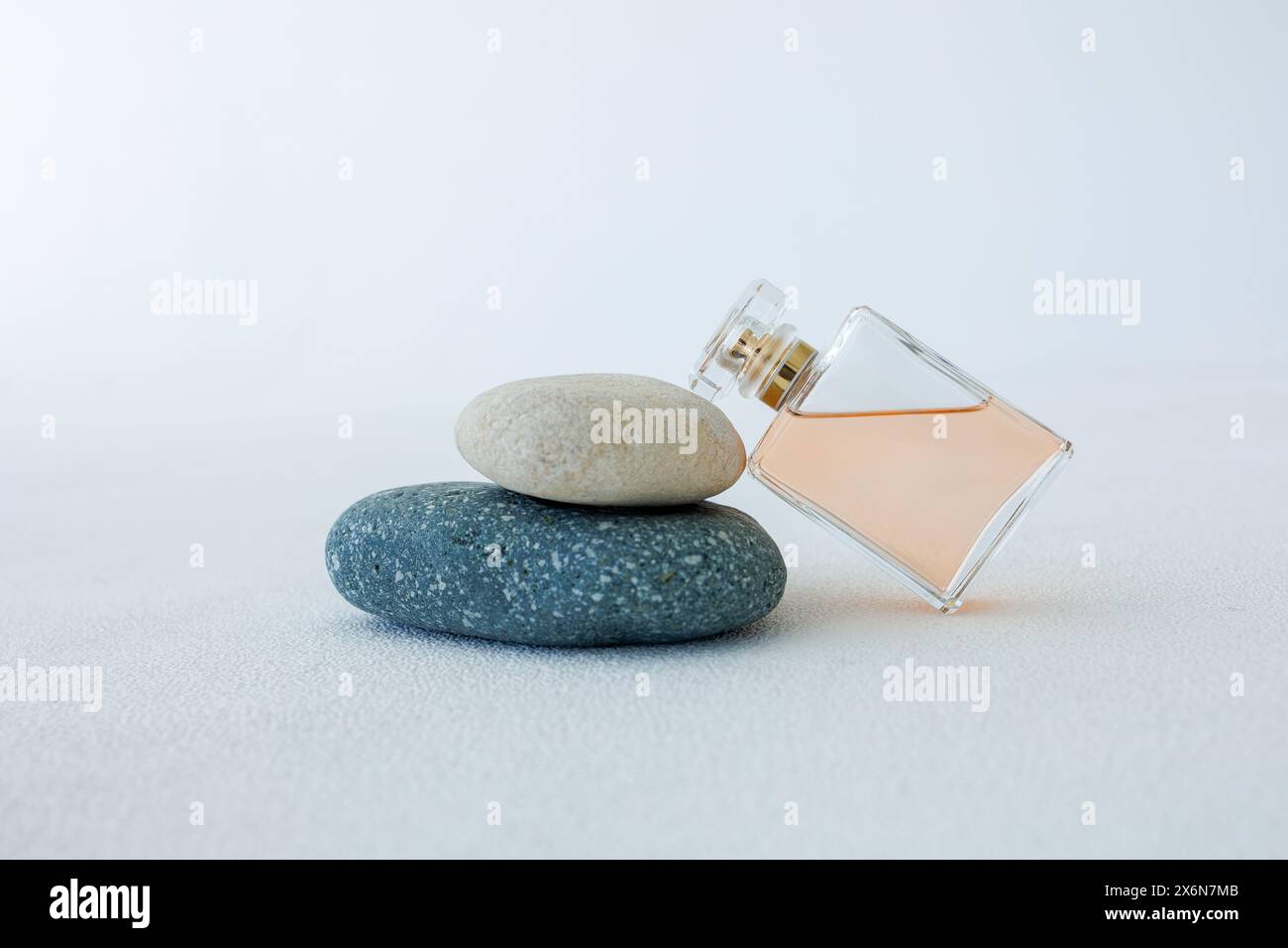 Flasche Parfüm auf Steinen auf weißem Hintergrund. Duftpräsentation bei Tageslicht. Konzept in Naturmaterialien Stockfoto