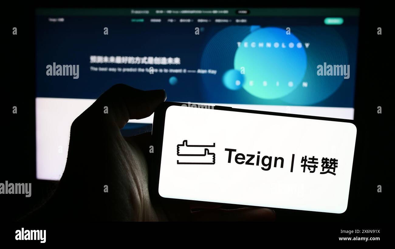 Person, die ein Mobiltelefon mit dem Logo des chinesischen Content Analytics-Unternehmens Tezign vor der Business-Webseite hält. Schwerpunkt auf dem Display des Telefons. Stockfoto