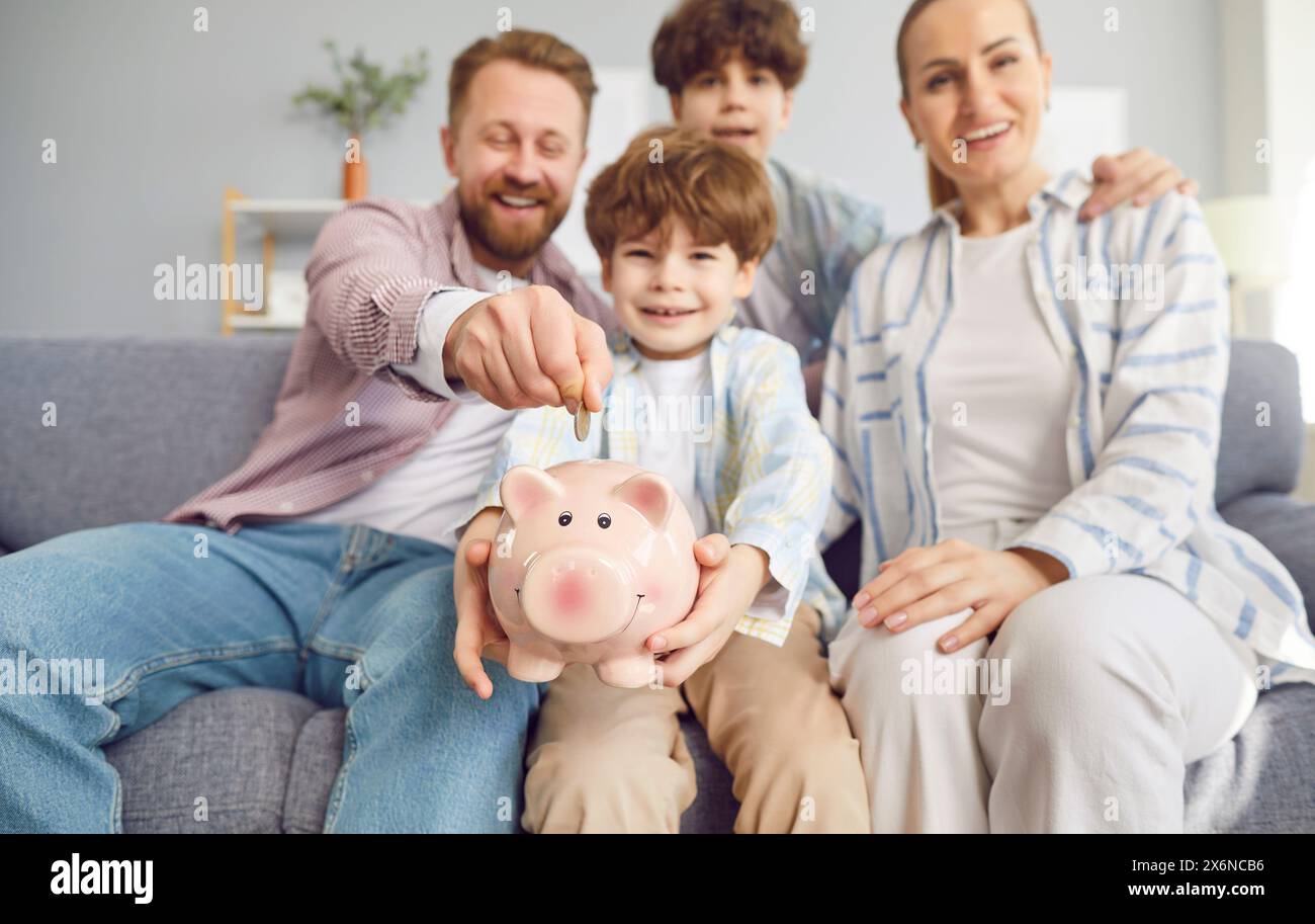 Lächelnde Familie, Eltern Mit Kindern, Die Coin In Piggy Bank Stecken Stockfoto