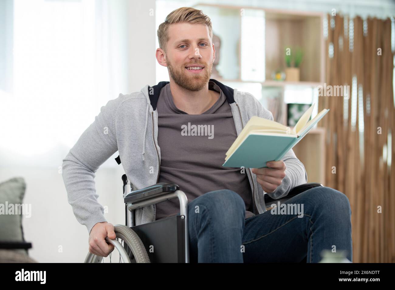 Ein selbstbewusster behinderter Mann im Rollstuhl mit einem Buch Stockfoto