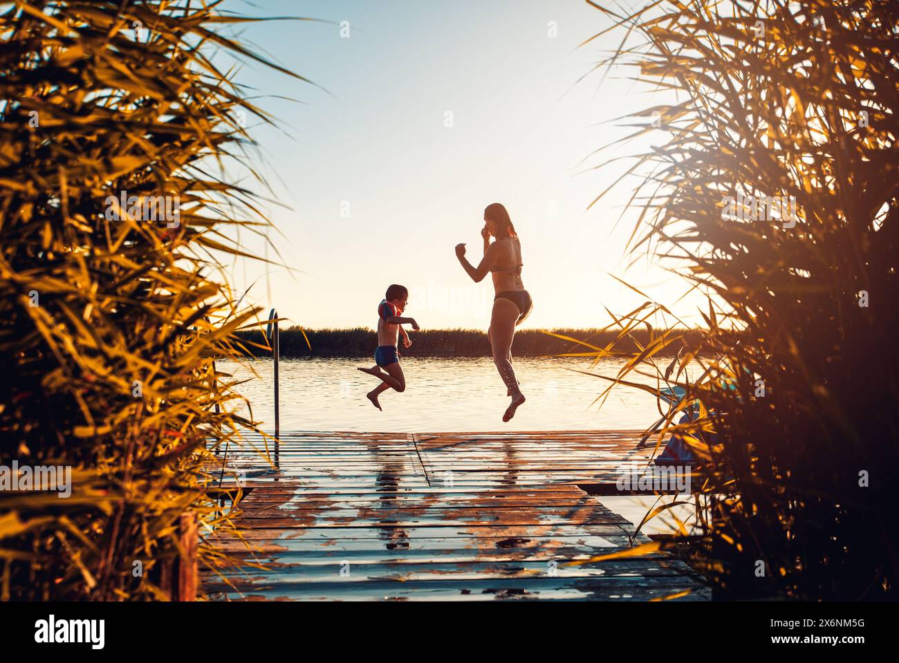Alleinerziehende Mutter mit ihrem Sohn, die am Sommertag vom Pier aus im See springt. Stockfoto