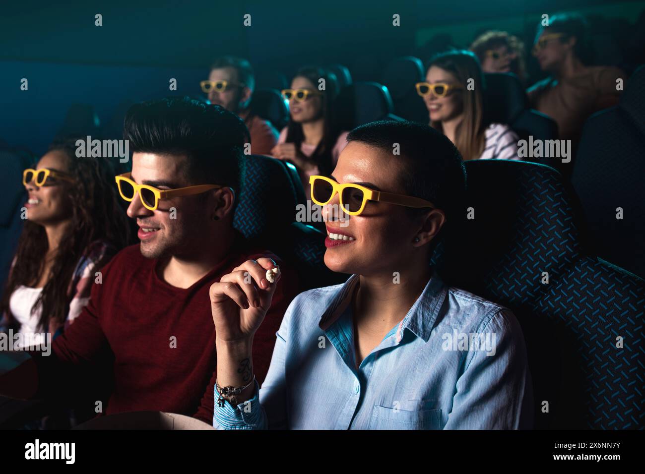 Eine Gruppe fröhlicher Menschen lacht, während sie mit einer 3D-Brille Filme im Kino anschauen. Stockfoto
