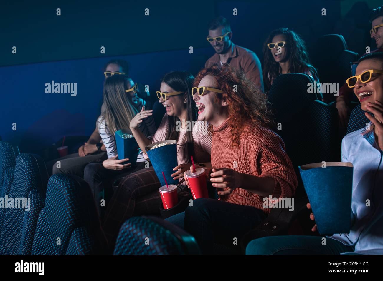 Eine Gruppe fröhlicher Menschen lacht, während sie mit einer 3D-Brille Filme im Kino anschauen. Stockfoto