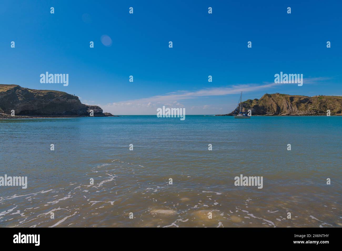 Lulworth Cove, Dorset, an einem schönen sonnigen Apriltag mit hellblauem Himmel und Meer, Felsen mit Nackenbarren und kalkhaltigen Klippen, ein paar kleine Yachten Stockfoto