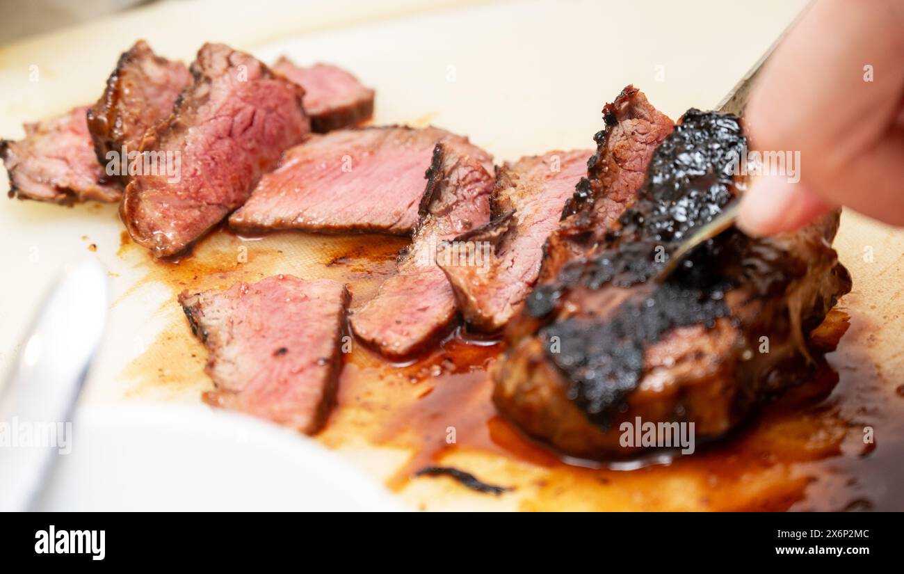Eine Person schneidet sorgfältig ein wunderschön gekochtes Steak, das seine zarte, rosa Mitte enthüllt. Der Schwerpunkt liegt auf der Textur und Sukkulenz des Fleisches Stockfoto