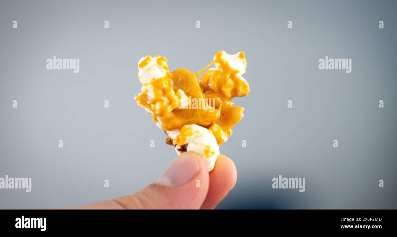 Eine Person hält eine Gruppe karamellbeschichtetes Popcorn, das vor einem gedämpften blauen Hintergrund präsentiert wird und die Textur und goldene Farbe des Snacks betont. Stockfoto