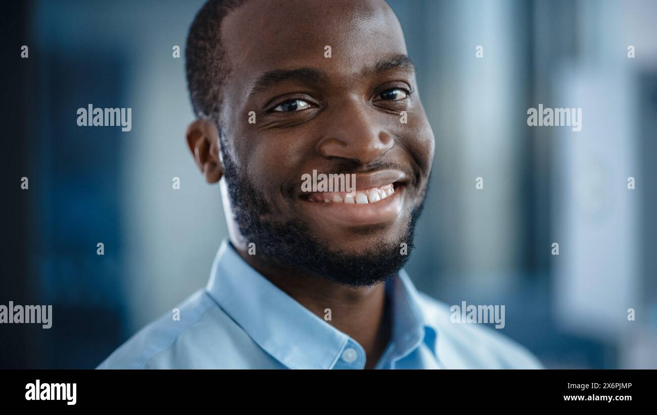 Nahaufnahme Porträt eines gutaussehenden Schwarzen Afroamerikaners in einem hellblauen Freizeitshirt. Erfolgreicher Mann lächelt ruhig, während er die Kamera ansieht. Glücklicher stilvoller Geschäftsmann oder Arzt im Krankenhaus. Stockfoto