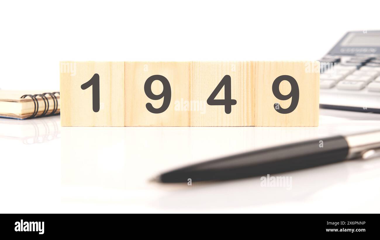 Die Zahlen 1949 auf Holzwürfeln geschrieben in einer Komposition mit einem Taschenrechner, einem Stift auf weißem Hintergrund Stockfoto