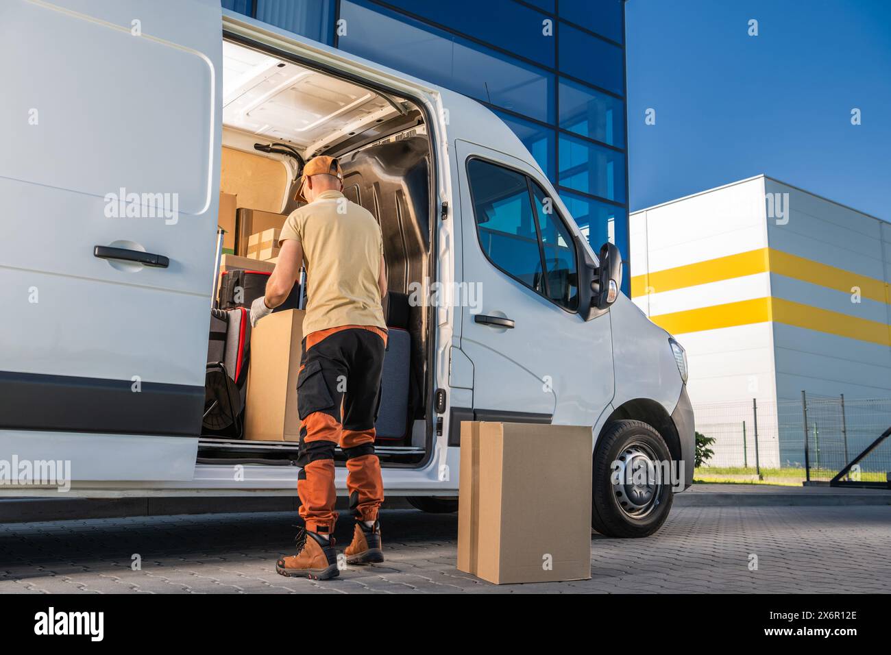Der Kurier steht am weißen, fahrenden Van, öffnet die Tür. Paketzustellung an einen Kunden Stockfoto