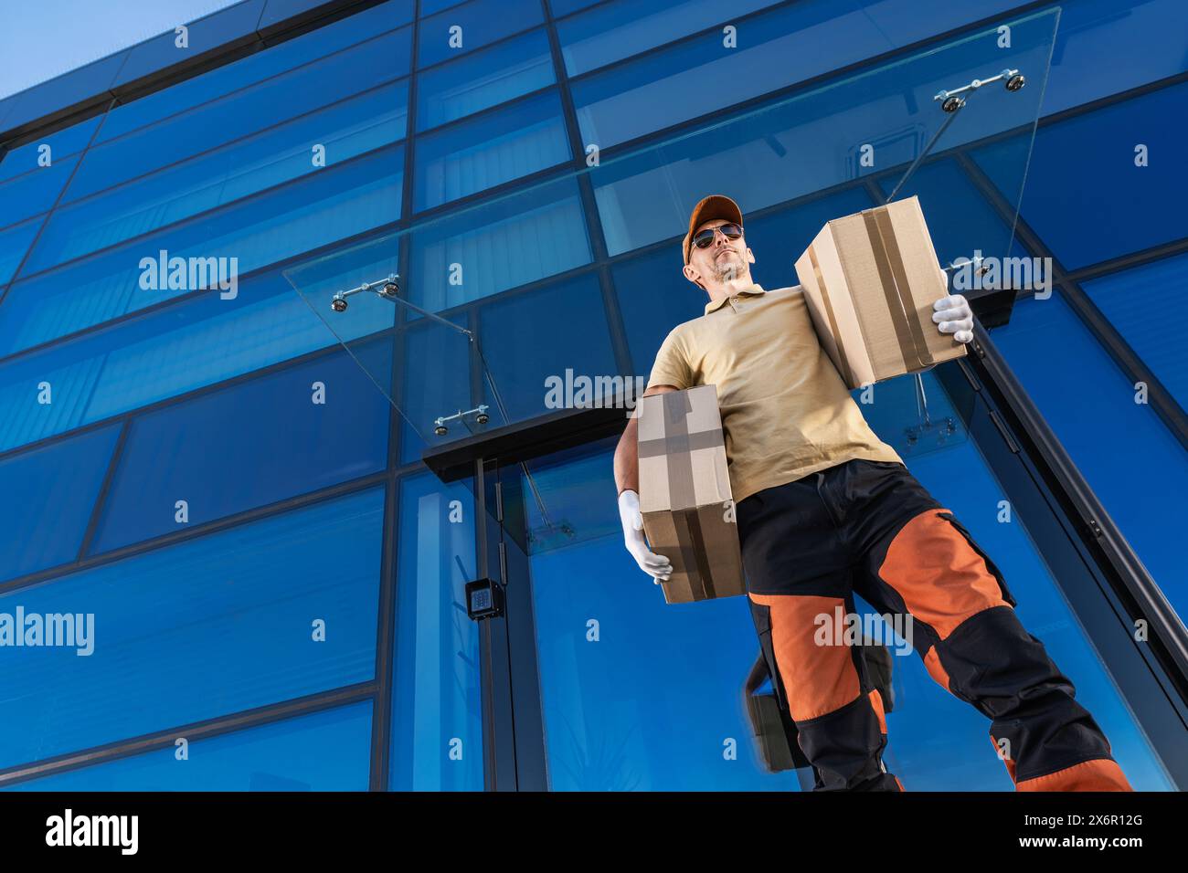 Ein kaukasischer Kurier steht mit einem Paket in der Hand vor einem Gebäude. Stockfoto