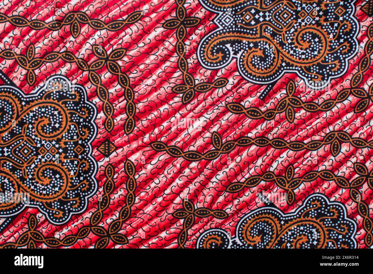 Draufsicht auf rot-gelben ankara-Stoff, flaches nigerianisches Wachstuch mit Motiven, ausgebreitetes rot-gelbes ankara-Material Stockfoto