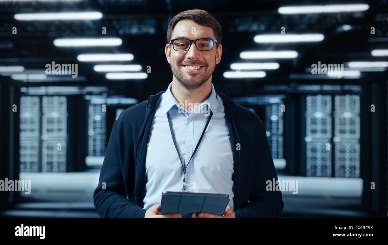 Porträt eines bärtigen, gutaussehenden kaukasischen IT-Spezialisten für Brillen, der mit Tablet steht und in der Mitte eines funktionierenden Serverraums eines Rechenzentrums posiert, in dem Servercomputer auf einem Rack arbeiten. Stockfoto