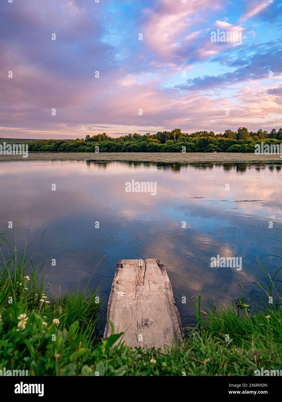 Wunderschöner rosa Sonnenuntergang über dem ruhigen See am Abend auf dem Land. Ruhiger See mit einem hölzernen Dock im Vordergrund. Stockfoto