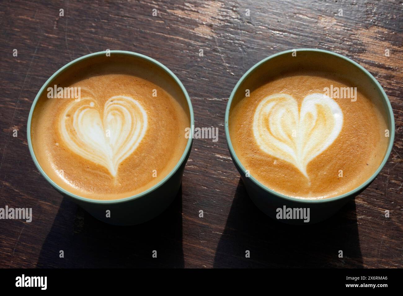 Zwei wiederverwendbare Tassen mit Cappuccino auf einem Holztisch in Nahaufnahme Stockfoto