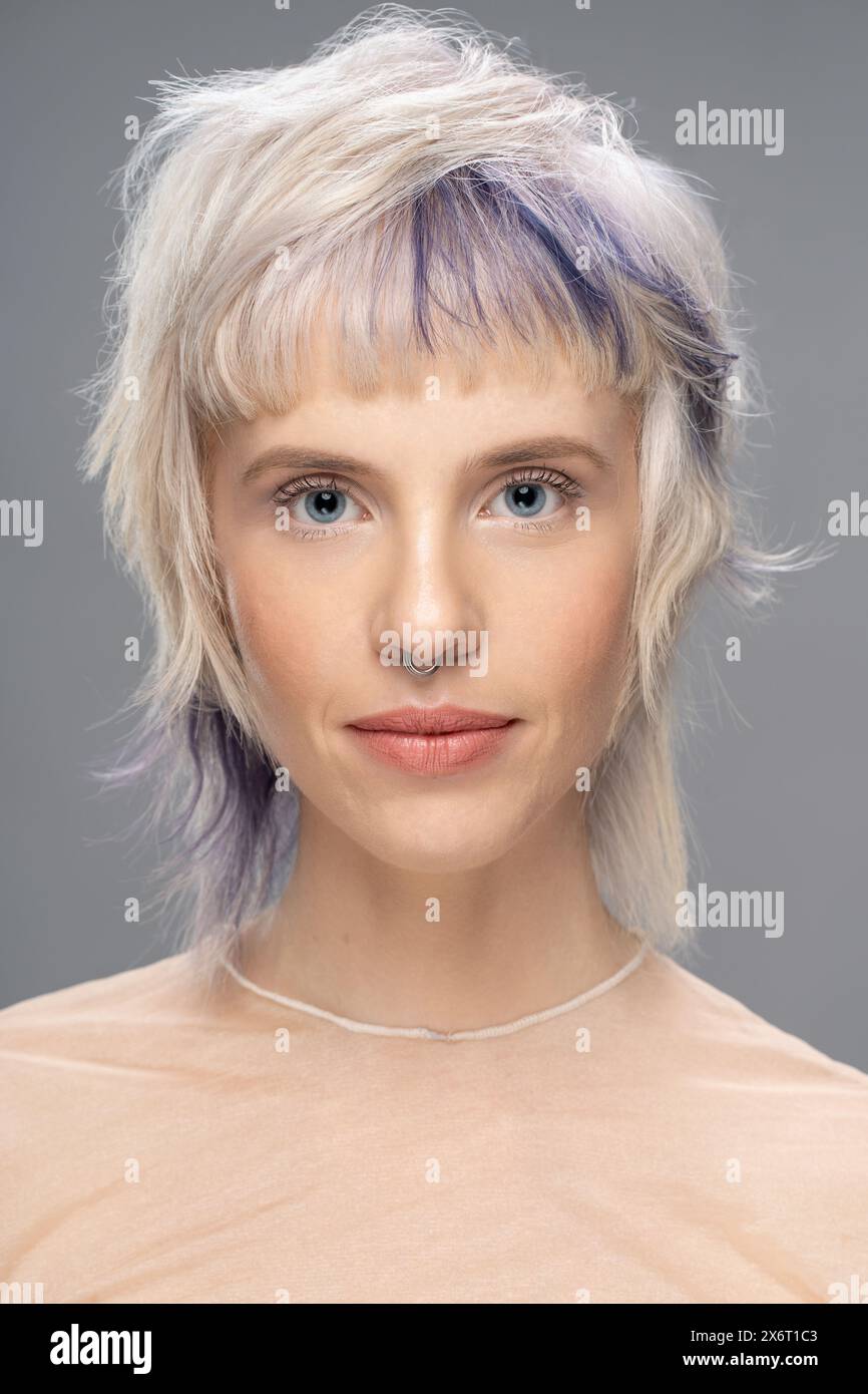 Nahporträt einer jungen Frau mit blondem und gefärbtem Haar, Septumpiercing und transparentem Oberteil. Moderne Frisur und Make-up, Mode Stockfoto