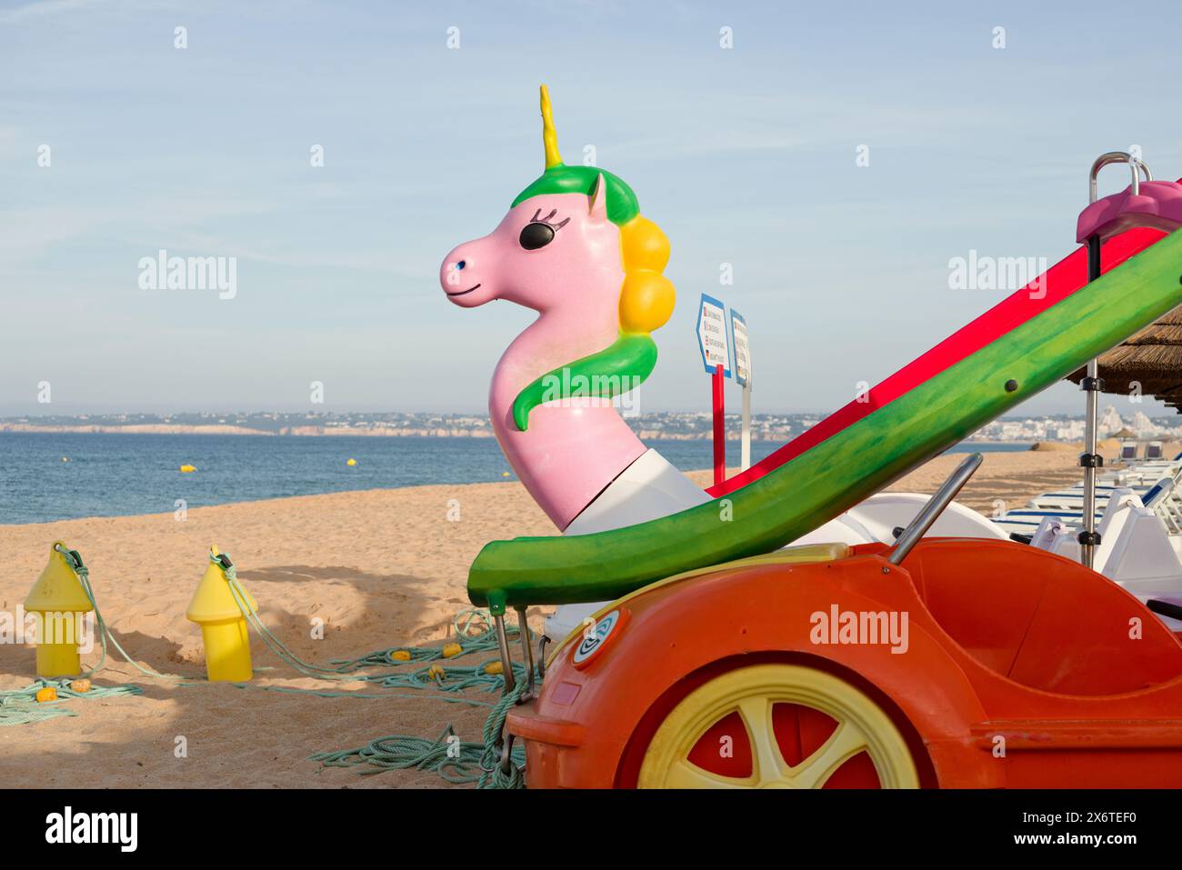 Tretboote am Strand. Einhorn in Pink mit rotem Auto und grüner Rutsche. Tretboot für Strand- und Strandunterhaltung. Stockfoto