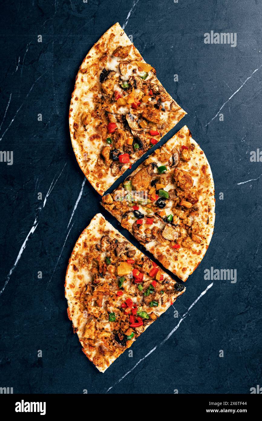 Gourmet-Pizzascheiben mit Gemüse und Huhn auf dunklem Hintergrund Stockfoto