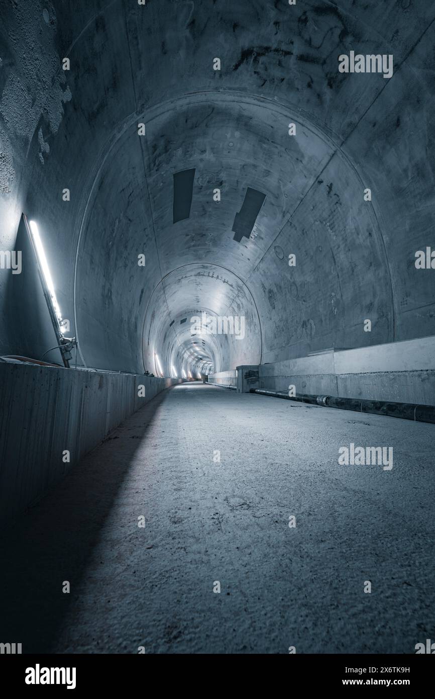 Ein langer, karger Tunnel mit minimalistischer Beleuchtung und Betonwänden, der eine kalte und raue Atmosphäre ausstrahlt, Tunnelbau Hermann Hesse Bahn Stockfoto